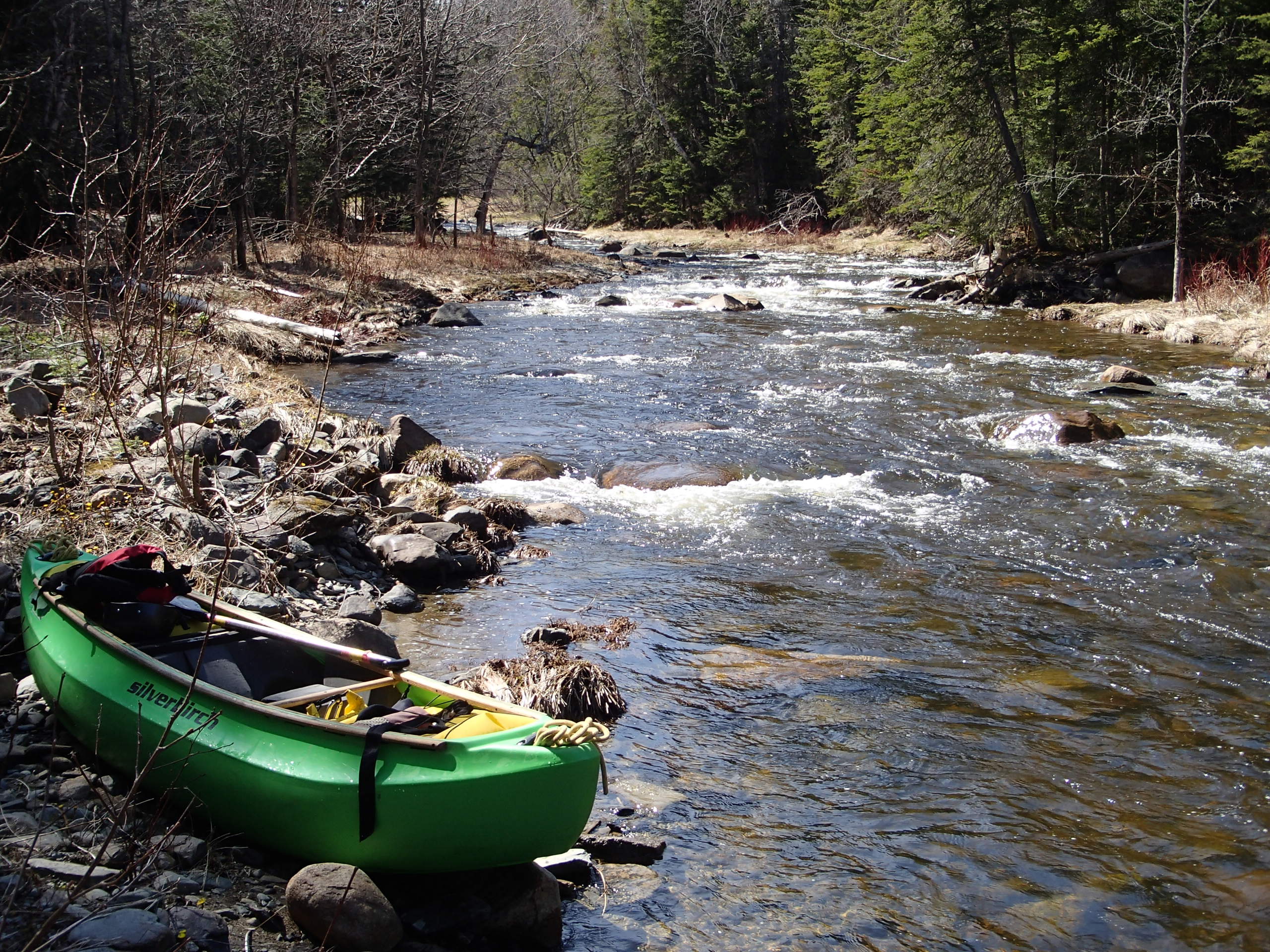 Vue sur une rivière, temps ensoleillé, un kayak vide au premier plan