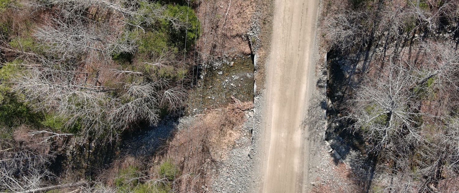 Vue aérienne sur un chemin en milieu forestier traversant un cours d'eau. 