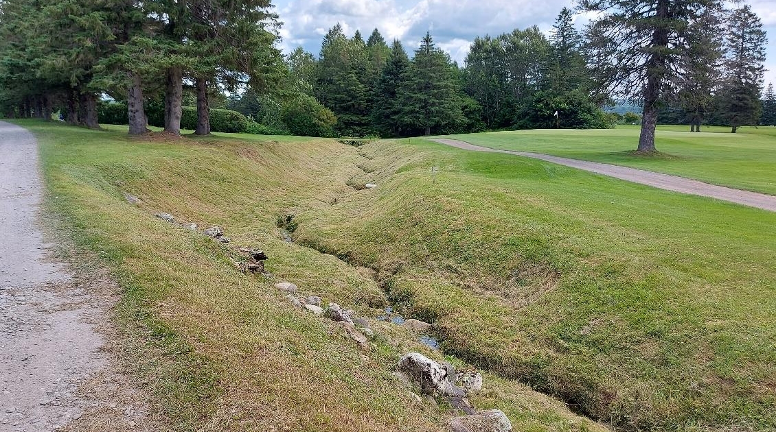 Golf-Ste-Marie_cours-deau_2021 Vue sur un ruisseau qui longe un sentier de terrain de golf. Les rives du ruisseau sont engazonnées et lui donnent un aspect artificiel. Projet de restauration du cours d'eau en cours