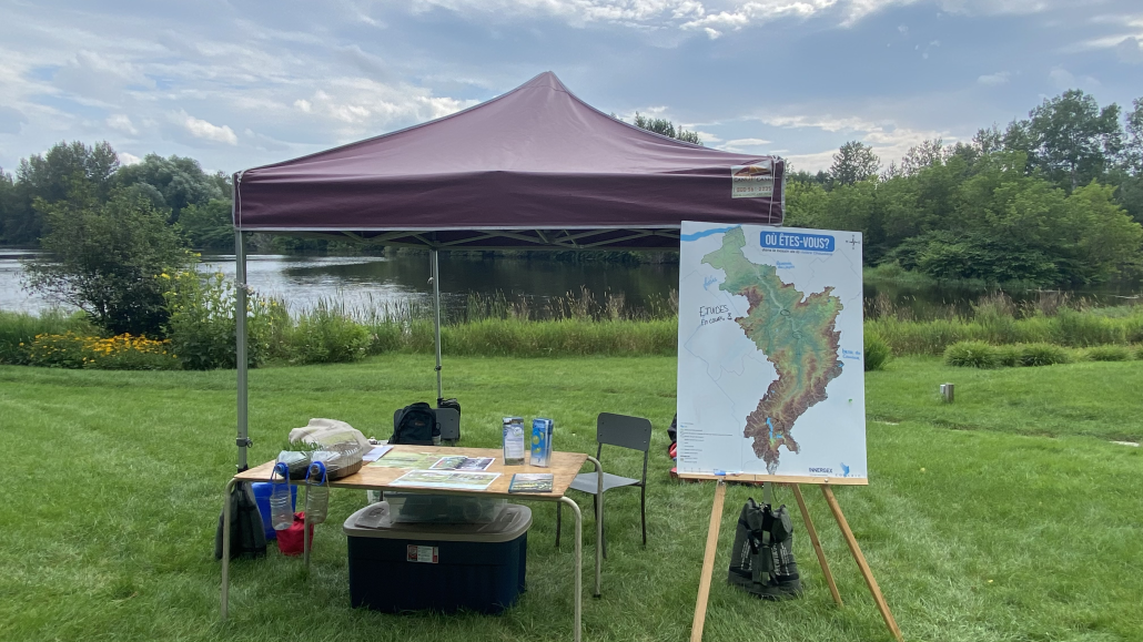 Kiosque dans un parc au bord de l'eau avec chapiteau, maquette et carte du territoire.