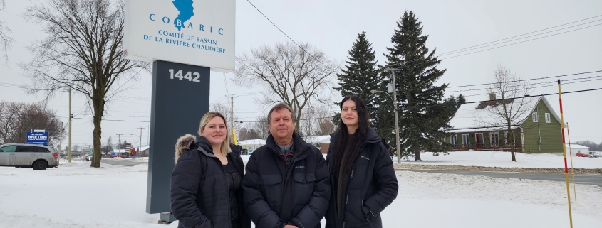 Sur le bord de la route Kennedy à Scott, Véronique Brochu, Luc Proulx et Sofianne Bouchard-Verret posent sous l'enseigne indiquant l'emplacement des bureaux du Comité de bassin de la rivière Chaudière